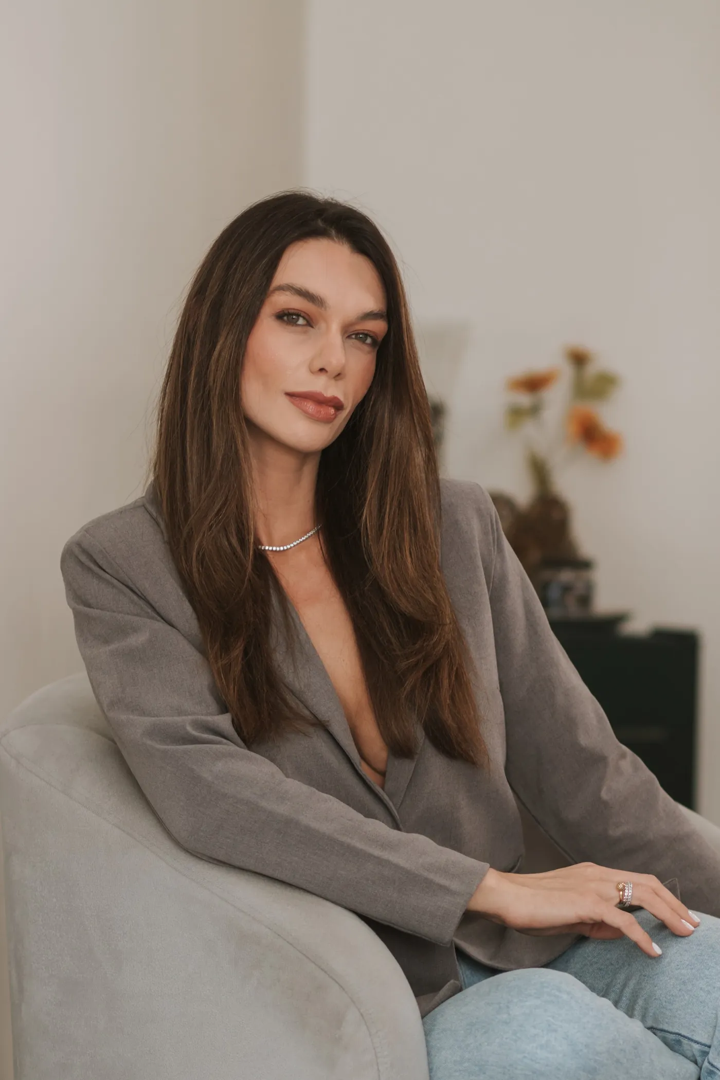 Dra. Stella Cardoso de blazer cinza, sentada em uma sala clara.